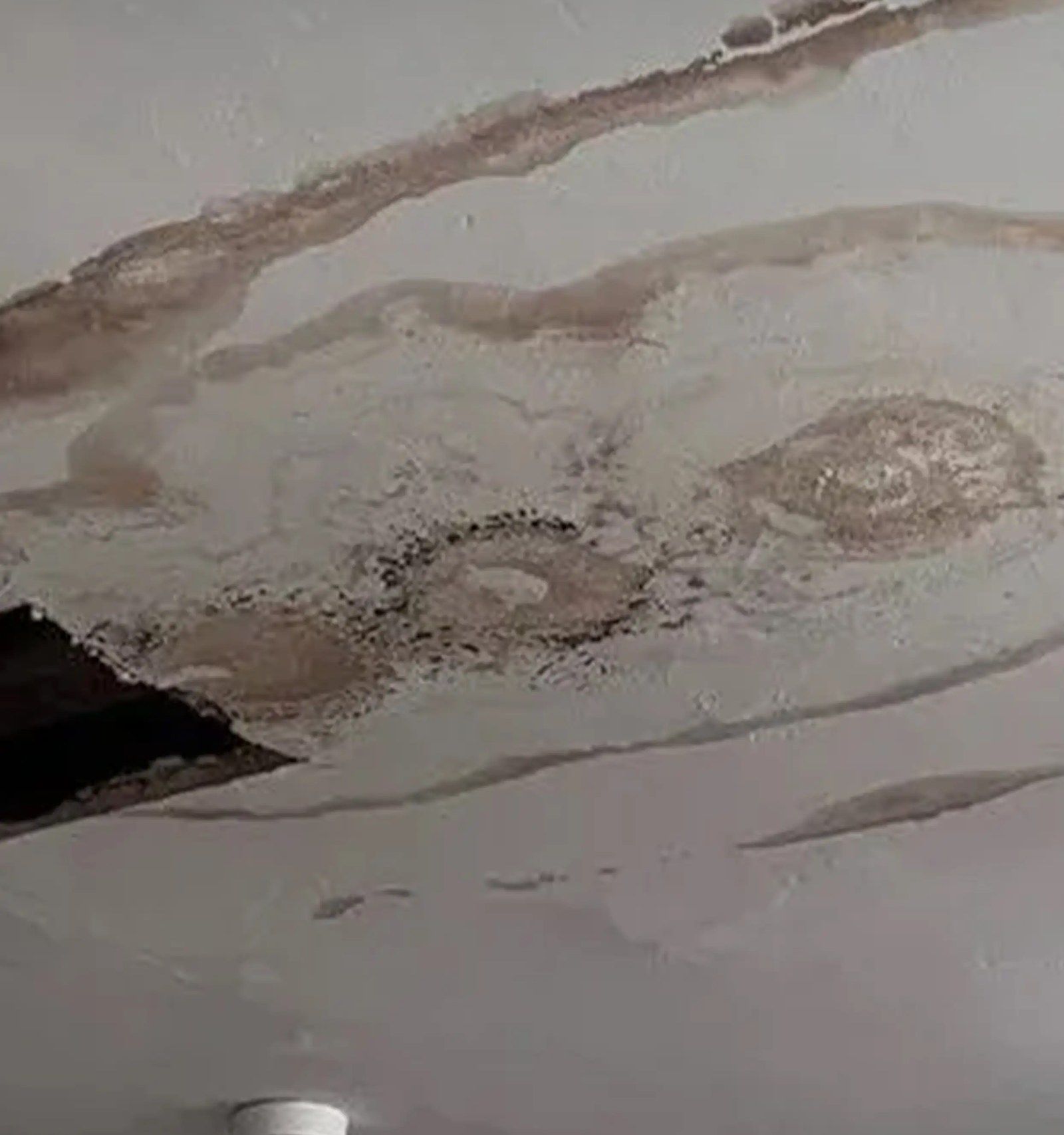 A ceiling with brown water stains and a hole where the plaster has come away