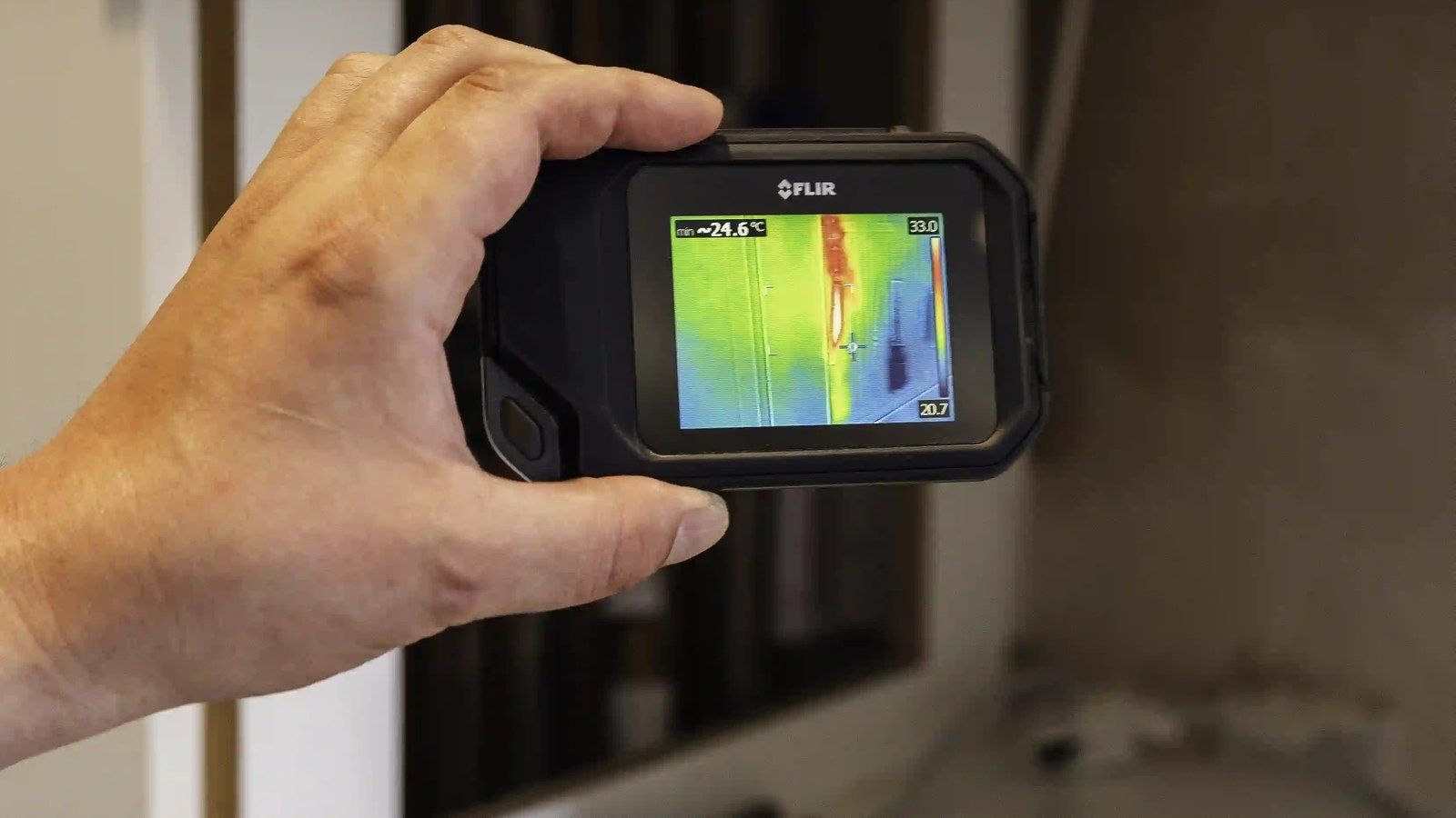 A hand holding a thermal imaging camera, its screen showing a warm yellow and red streak
